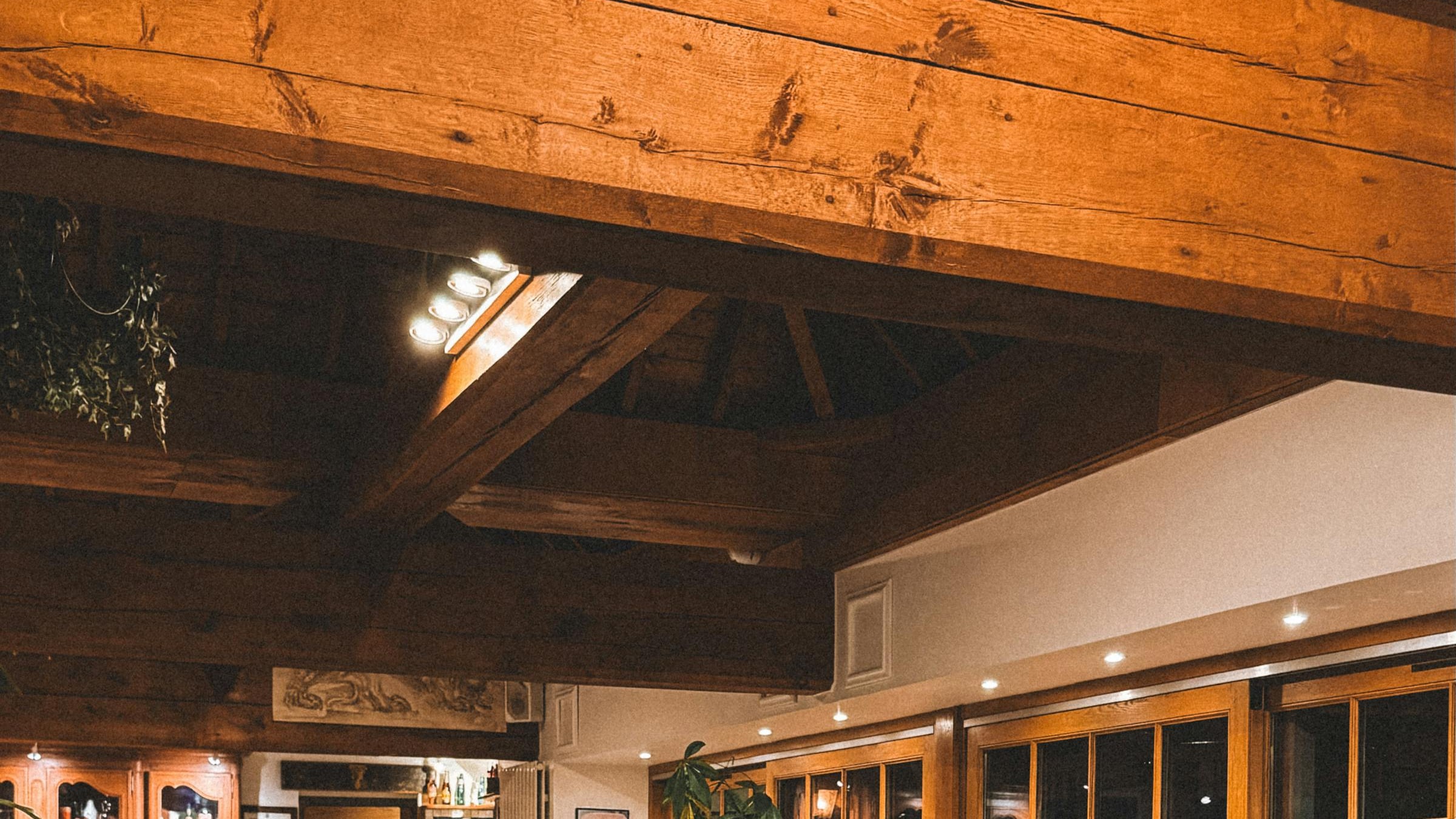 Warm commercial restaurant interior with an exposed timber-beam ceiling and wood-framed windows