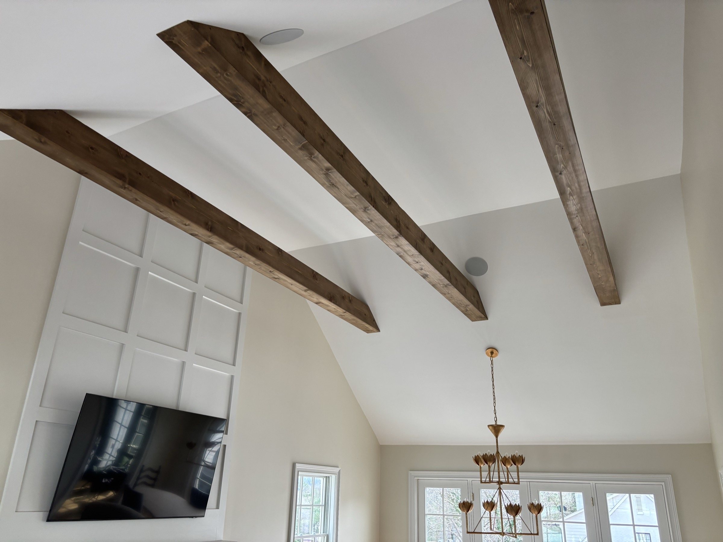 Vaulted great room with stained box beams and a paneled accent wall installed by Dunn Trim Co.