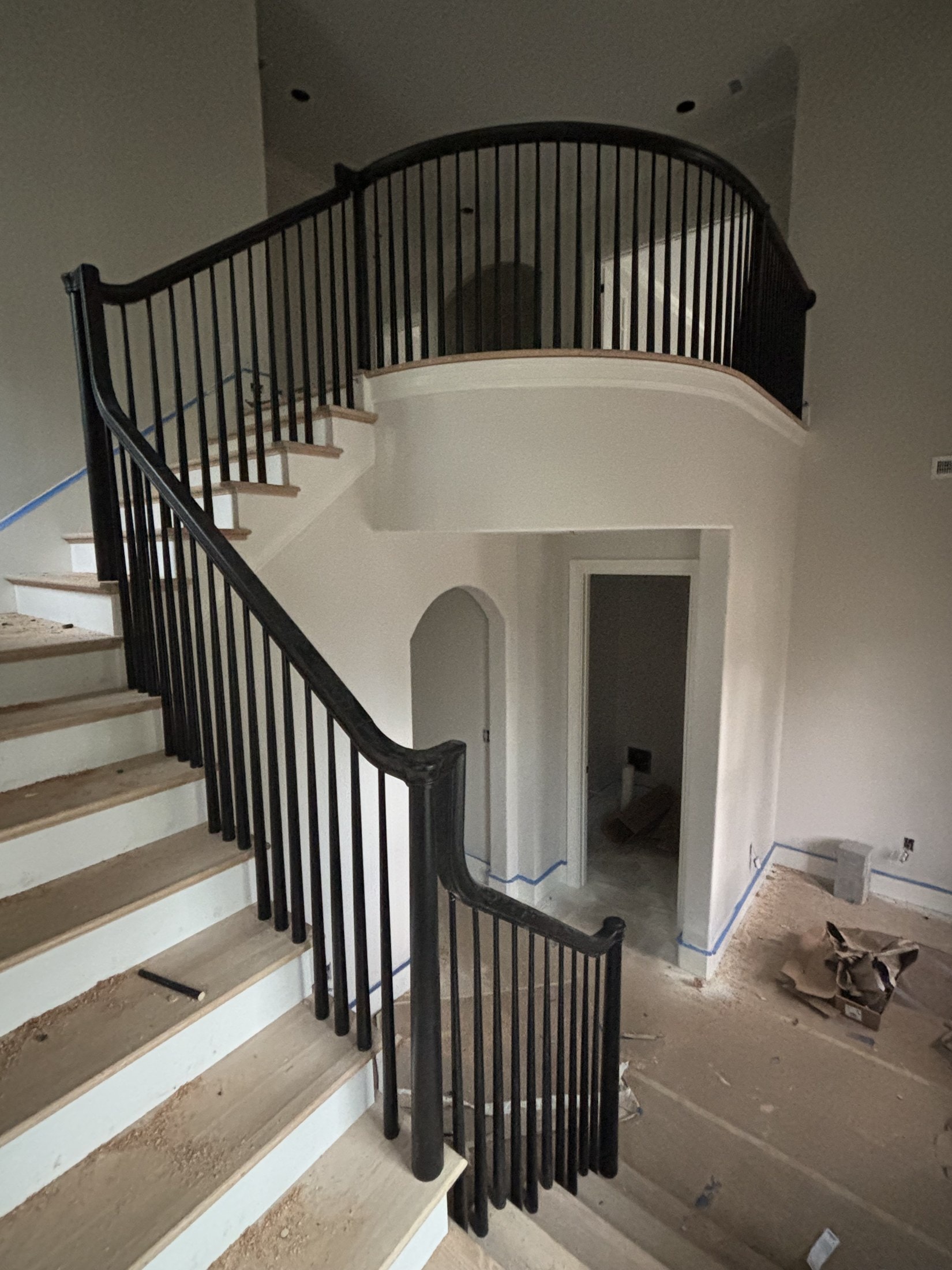 Curved staircase with wood treads, painted risers, and iron balusters