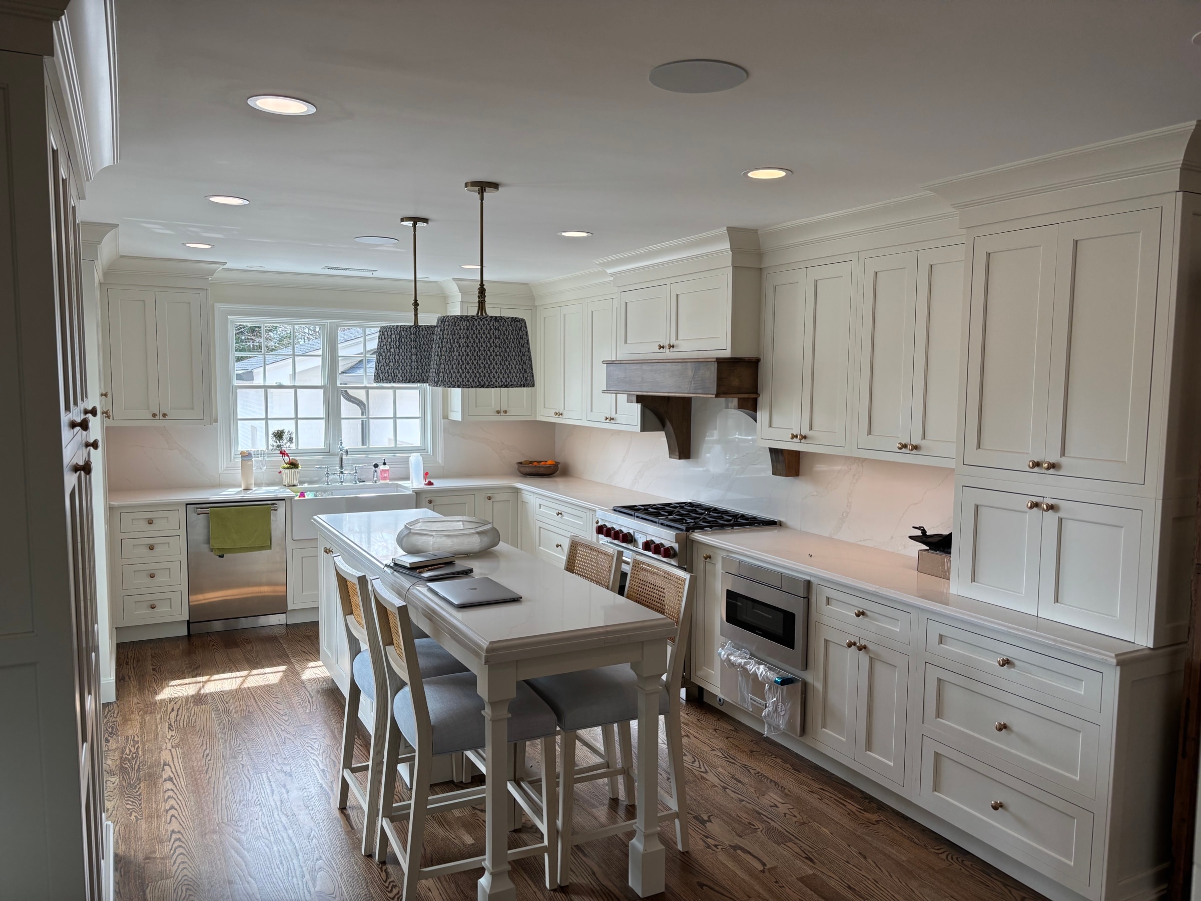 White kitchen with a custom wood range hood and a marble backsplash, installed by Dunn Trim Co.